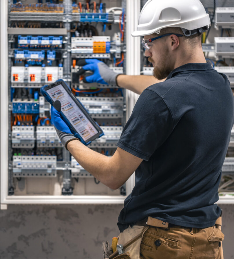 Electrical technician working in a switchboard with fuses, uses a tablet. Electrical technician looking focused while working in a switchboard with fuses. SSUCv3H4sIAAAAAAAACpySwW6DMAyG75P2DijnIgGBju5Vqh1MSMFqmlRJ6DRVffc5CaDsOnHBn+3f/jHP97eiYAM4FOyzeIaIYlRqcd6CR6MJV4eVW6lHaXPysPxY5QAwj+SI3lgElcMBvJg13CRBvSgV8CsmmfPgFydd2GVFArycSCPBXSItfE5xsSVikjooxdghY24ZIttQEv9XZ3r52g1PUoufuHBmxEolIRk5p1J2/fbS3nJrsIxoMlcPI0CFAp4pAd7Bwp++u0WBesqI8XO8y6YkzKK9DVvtZpgy5g6DCl/9QmPkxmdwjsrHjWezBf0F5pbN0cZHT6sqG+k4Iaw5747NBz193fZN1ZzWgnTQGUknrrMJUSyuOOauMGxAJzi1XVdBCU3Ly7aq67Lvu65seNe3cOLHgV/oFq9fAAAA//8DAIlQOhS5AgAA
